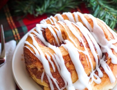 Lion House Cinnamon Roll on a white plate on top of a christmas table cloth.