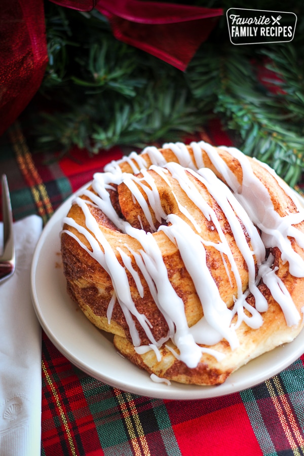 Lion House Cinnamon Roll on a white plate on top of a christmas table cloth.