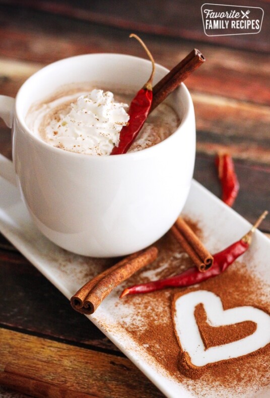 Mayan Hot Chocolate topped with whipped cream and cinnamon sticks in a white mug.