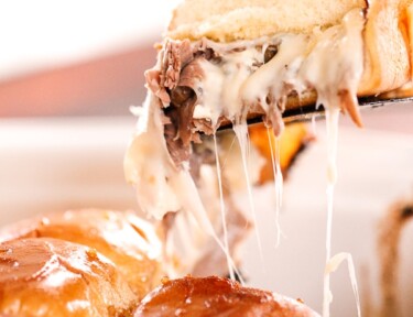 Mushroom Swiss Roast Beef Slider being scooped above the rest of the sliders with cheese dripping down the side.