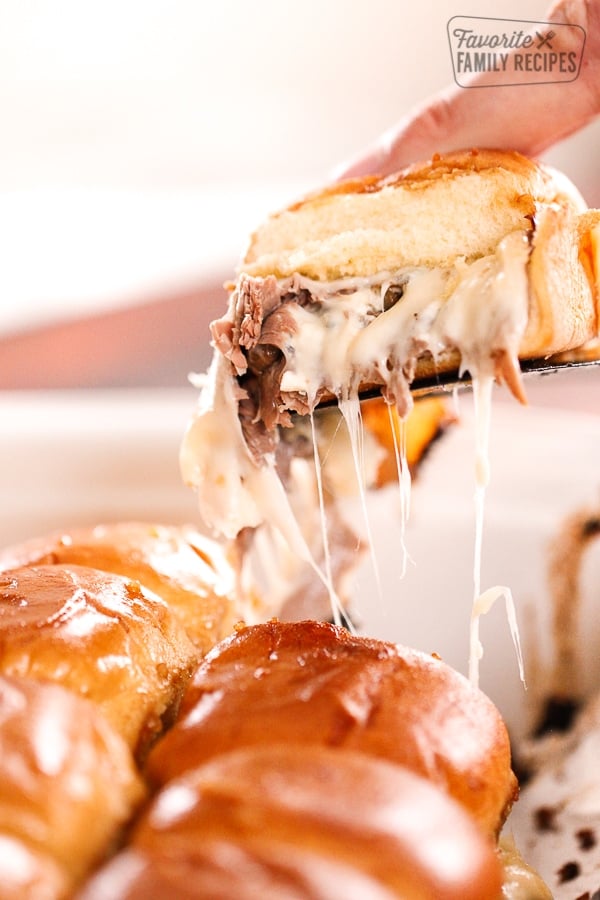 These Mushroom Swiss Roast Beef Sliders make the perfect appetizer! Tender beef with a tangy blue cheese horseradish sauce, these are to die for! Mushroom Swiss Roast Beef Slider being scooped above the rest of the sliders with cheese dripping down the side.