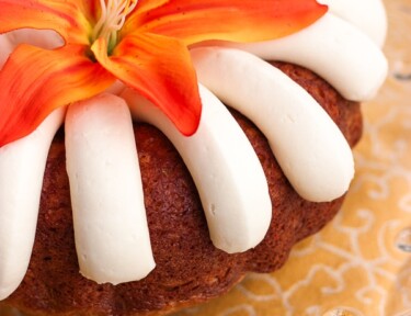 Nothing Bundt Cake’s Carrot Cake topped with an orange flower on a glass tray.