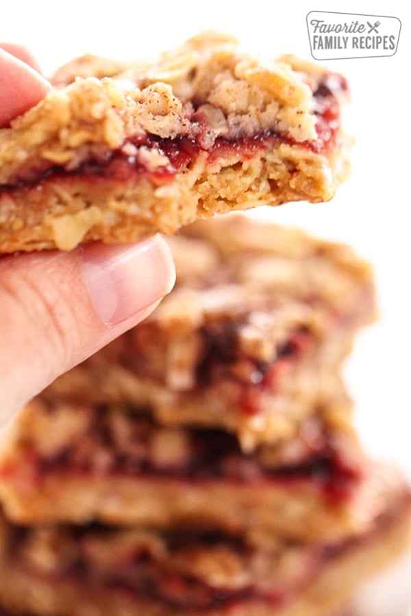Raspberry Oatmeal Crumb Bars are a sweet, buttery, fruity bar cookie with a nutty, crumbly crust. The perfect bar cookie for any occasion! Close up of a hand holding a Raspberry Oatmeal Bar with a bite taken out of it