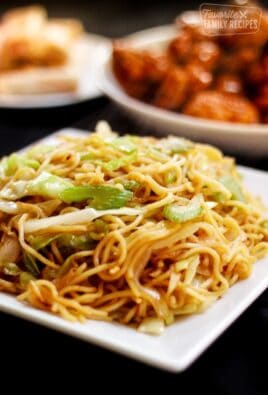 Panda Express Chow Mein in a white dish with orange chicken in the background.