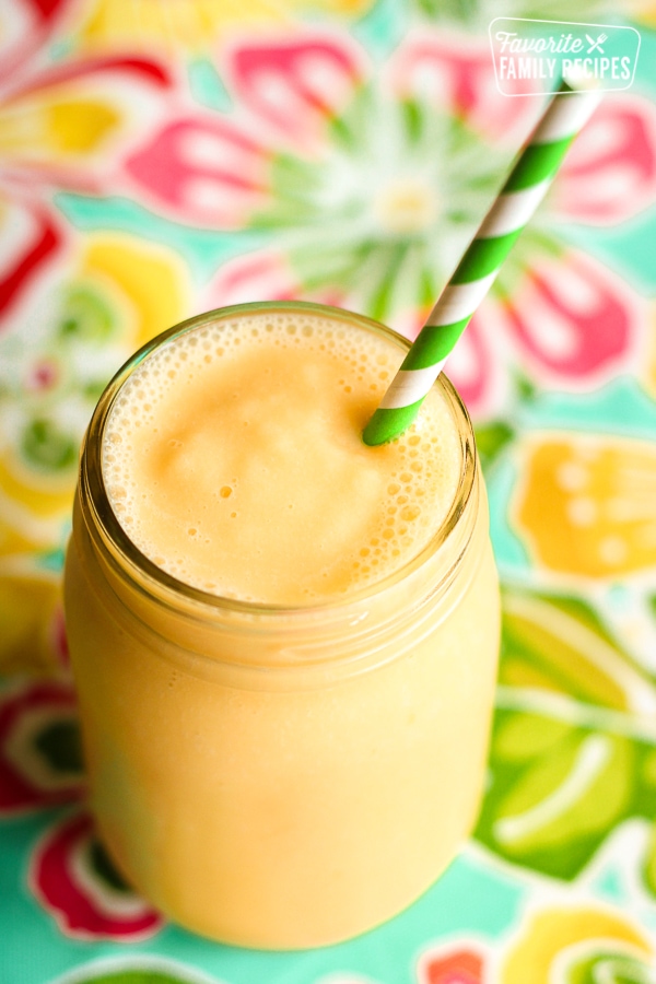 Peach smoothie in a jar with a green and white striped straw. 