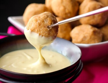 Peanut butter bon bons being dipped in sauce.