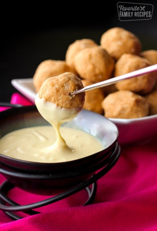 Peanut butter bon bons being dipped in sauce.