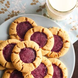 8 Peanut Butter and Jelly Cookies on a blue plate with a glass of milk on the side.