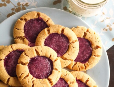 8 Peanut Butter and Jelly Cookies on a blue plate with a glass of milk on the side.