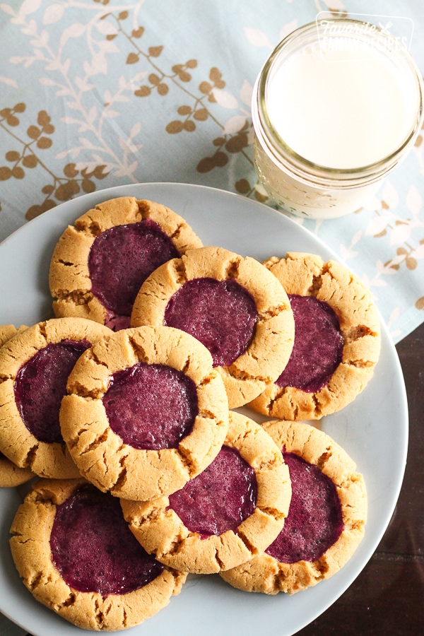 8 Peanut Butter and Jelly Cookies on a blue plate with a glass of milk on the side. 