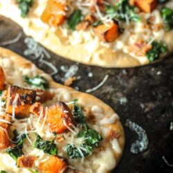 Roasted butternut squash pizza on a black plate.