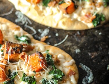 Roasted butternut squash pizza on a black plate.