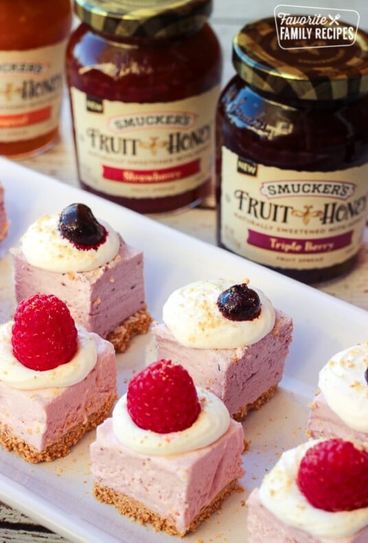 Cheesecake bites on a white tray with Smucker's Jam in the background