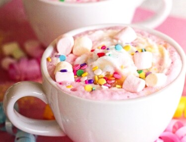 Two white mugs filled with Unicorn Hot Chocolate topped with mini marshmallows and sprinkles