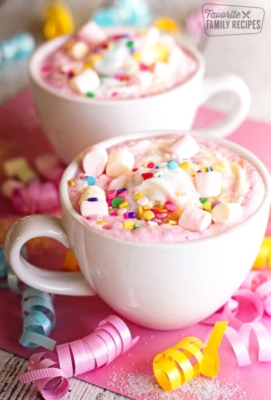 Two white mugs filled with Unicorn Hot Chocolate topped with mini marshmallows and sprinkles