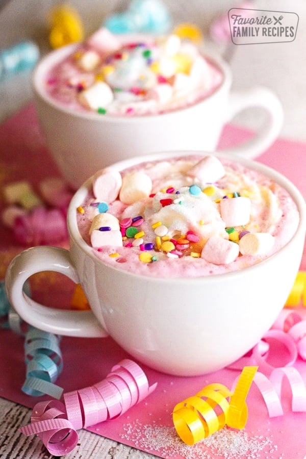 Two white mugs filled with Unicorn Hot Chocolate topped with mini marshmallows and sprinkles