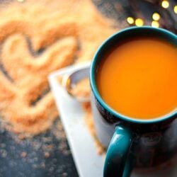 A cup of hot Wassail in a blue mug with Wassil mix on the counter next to it.