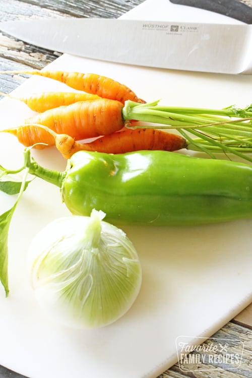 Carrots, a pepper, and an onion on a cutting board with a chef's knife