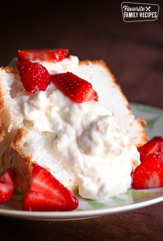 Slice of angel food cake covered in pineapple whip and slices of strawberries on a plate.