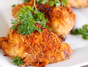 3 pieces of Paprika & Parmesan Chicken topped with a garnish on a white plate