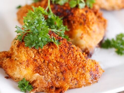 3 pieces of Paprika & Parmesan Chicken topped with a garnish on a white plate