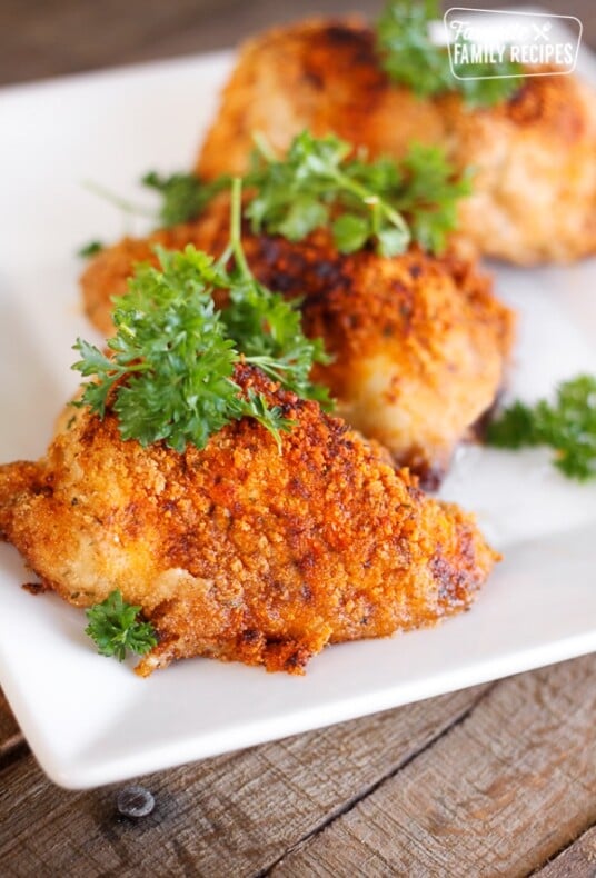 3 pieces of Paprika & Parmesan Chicken topped with a garnish on a white plate