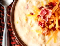 Bacon and Corn Chowder topped with cheese and bacon in a bowl with a spoon on the side.