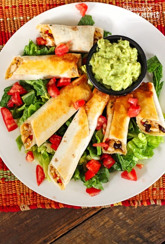 6 Baked Chicken Firecrackers on a plate with lettuce and tomatoes and a small black bowl of guacamole.