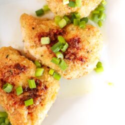 3 pieces of baked garlic chicken topped with green onions on a white plate.