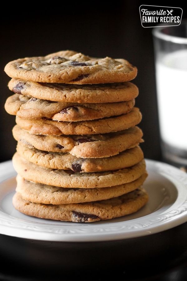 Bakery Chocolate Chip Cookies Stacked on a white Plate with a glass of milk in the background