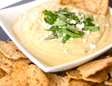 Basil Parmesan Hummus in a white Bowl with Crackers