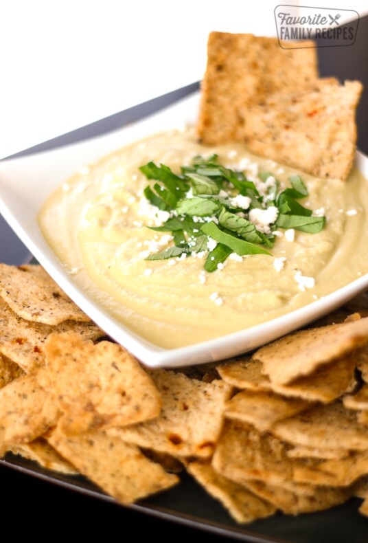 Basil Parmesan Hummus in a white Bowl with Crackers