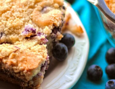 A piece of blueberry cream cheese coffee cake on a white serving plate with fresh blueberries