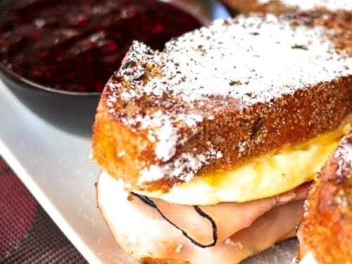 Breakfast Monte Cristos on a plate covered in powdered sugar with a bowl of jam in the background