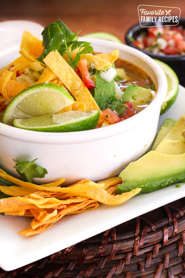 Cafe Rio Tortilla Soup in a white bowl with salsa, avocado, and tortilla strips on the side