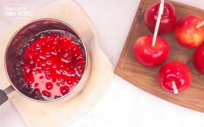 Candy apples on a wooden cutting board with candy apple syrup in a saucepan.