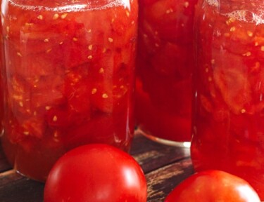 3 mason jars of Canned Diced Tomatoes with 2 fresh tomatoes on the side