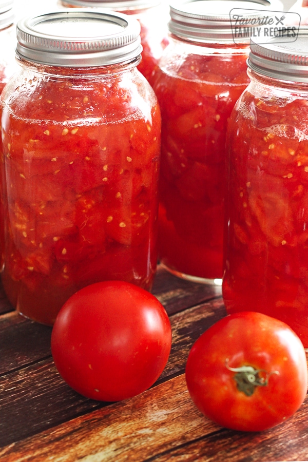 3 mason jars of Canned Diced Tomatoes with 2 fresh tomatoes on the side.