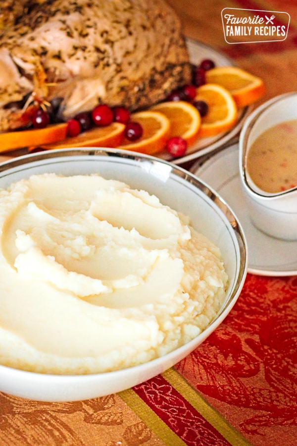 Cauliflower mashed potatoes in a white serving bowl with gravy and turkey in the background