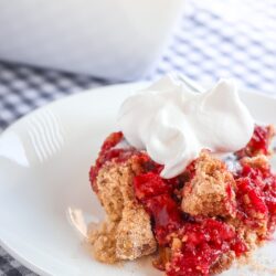 A piece Microwave Cherry Crunch topped with whipped cream on a white pate.