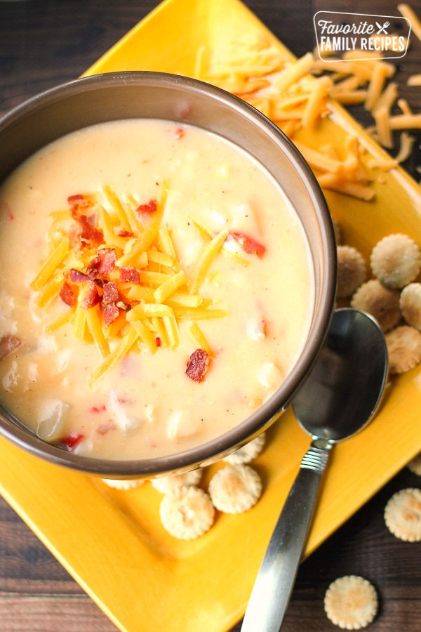 Chicken Cheddar Chowder in a bowl with cheese and bacon bits on top all on a yellow plate.