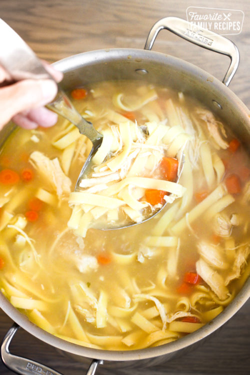 pot of chicken noodle soup with spoon stirring