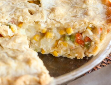 A chicken pot pie with vegetables in a pie plate with a slice cut out