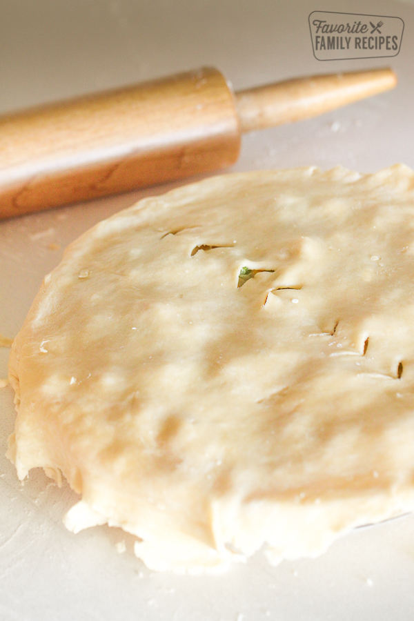 An uncooked chicken pot pie with the pie crust dough with decorative slits placed on top