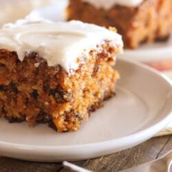 A slice of classic carrot cake on a white plate with another piece in the background.