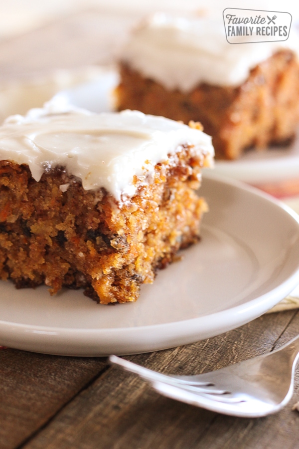 A slice of classic carrot cake on a white plate with another piece in the background.