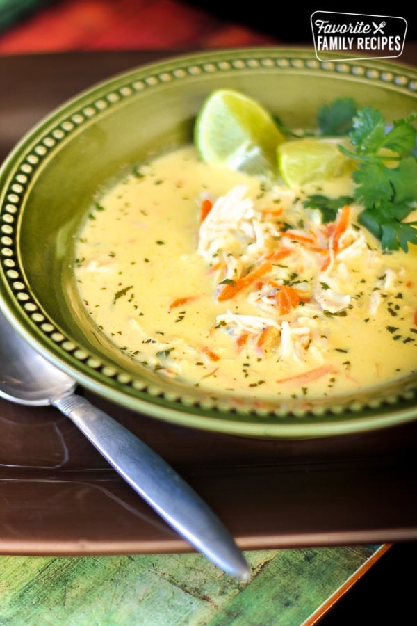 Thai Coconut Soup is full of sweet coconut, tangy lime and tender chicken. You'll love the bursts of sweet and savory flavor in this unique soup. Coconut Lime Chicken Soup in a green bowl with lime slices and cilantro.