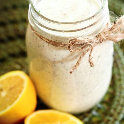 Creamy Basil Dressing in a mason jar with lemons on the side.