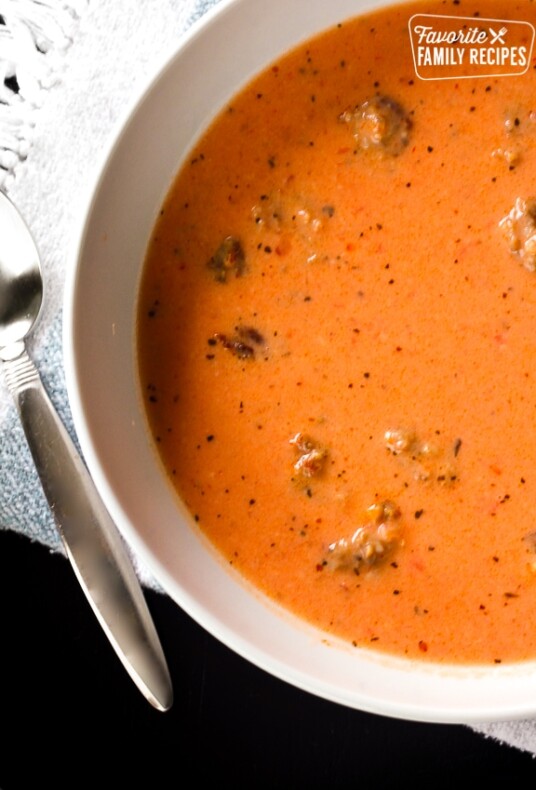 Creamy Tomato Basil Soup with Sausage in a white bowl with a spoon on the side.