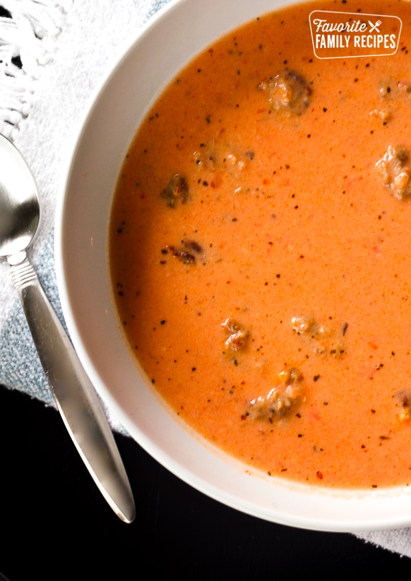 Creamy Tomato Basil Soup with Sausage in a white bowl with a spoon on the side.